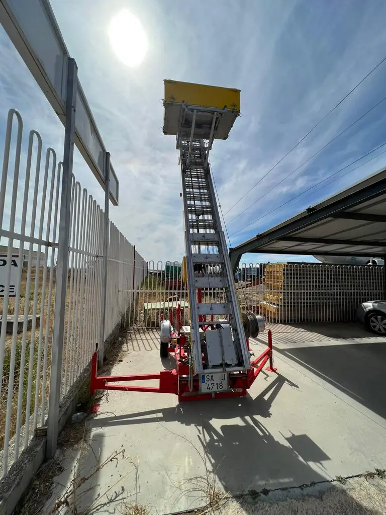 Plataforma elevadora de mudanzas desplegada en vertical junto a una valla, vista desde abajo