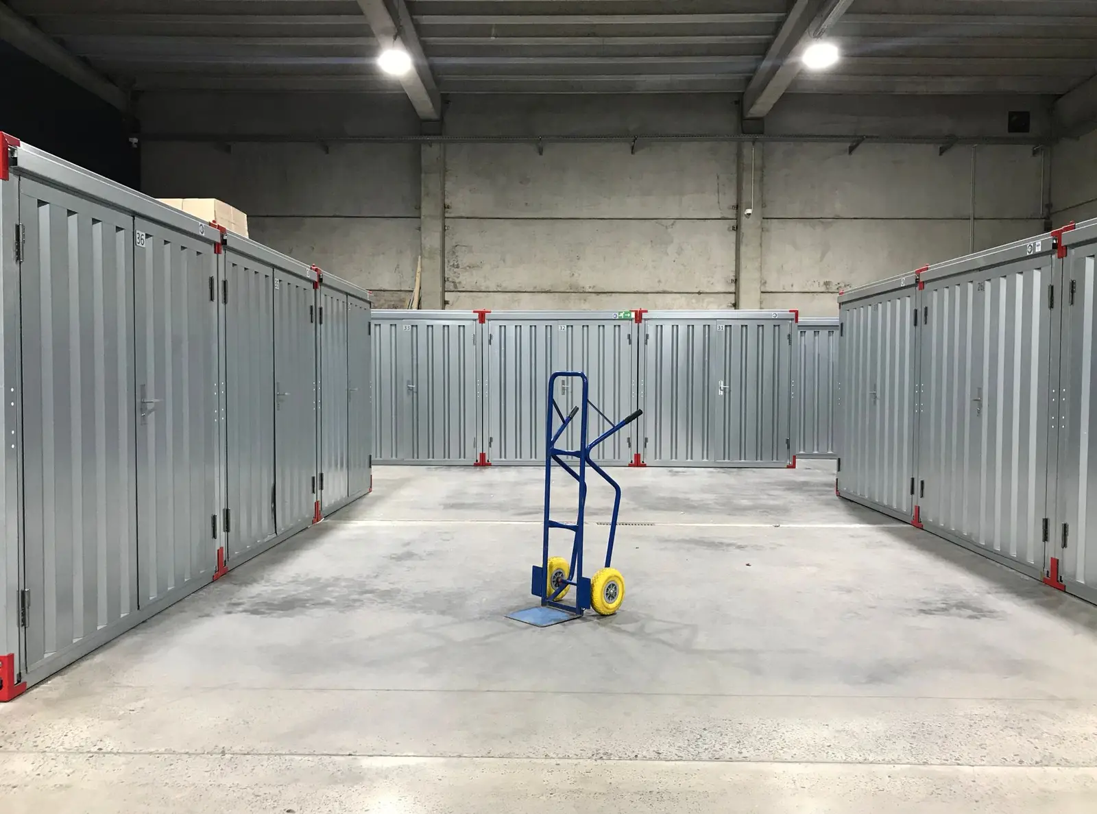 Pasillo de trasteros metálicos cerrados en una nave, con una carretilla en el centro