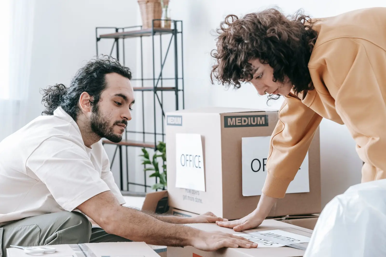 Dos personas etiquetan una caja de cartón marcada como oficina antes de un traslado